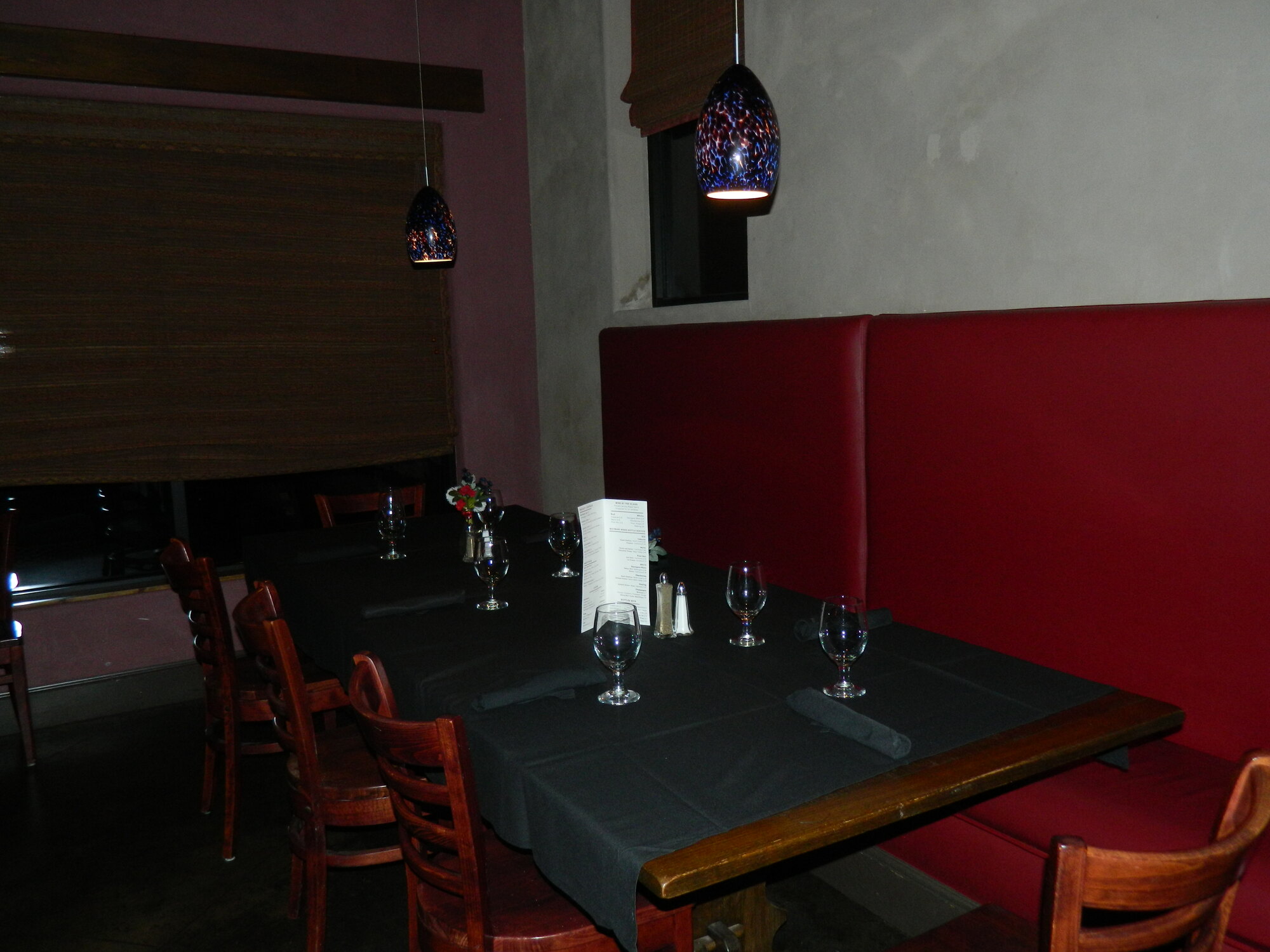 A dining table set beneath artisan pendant lights beside a red banquette